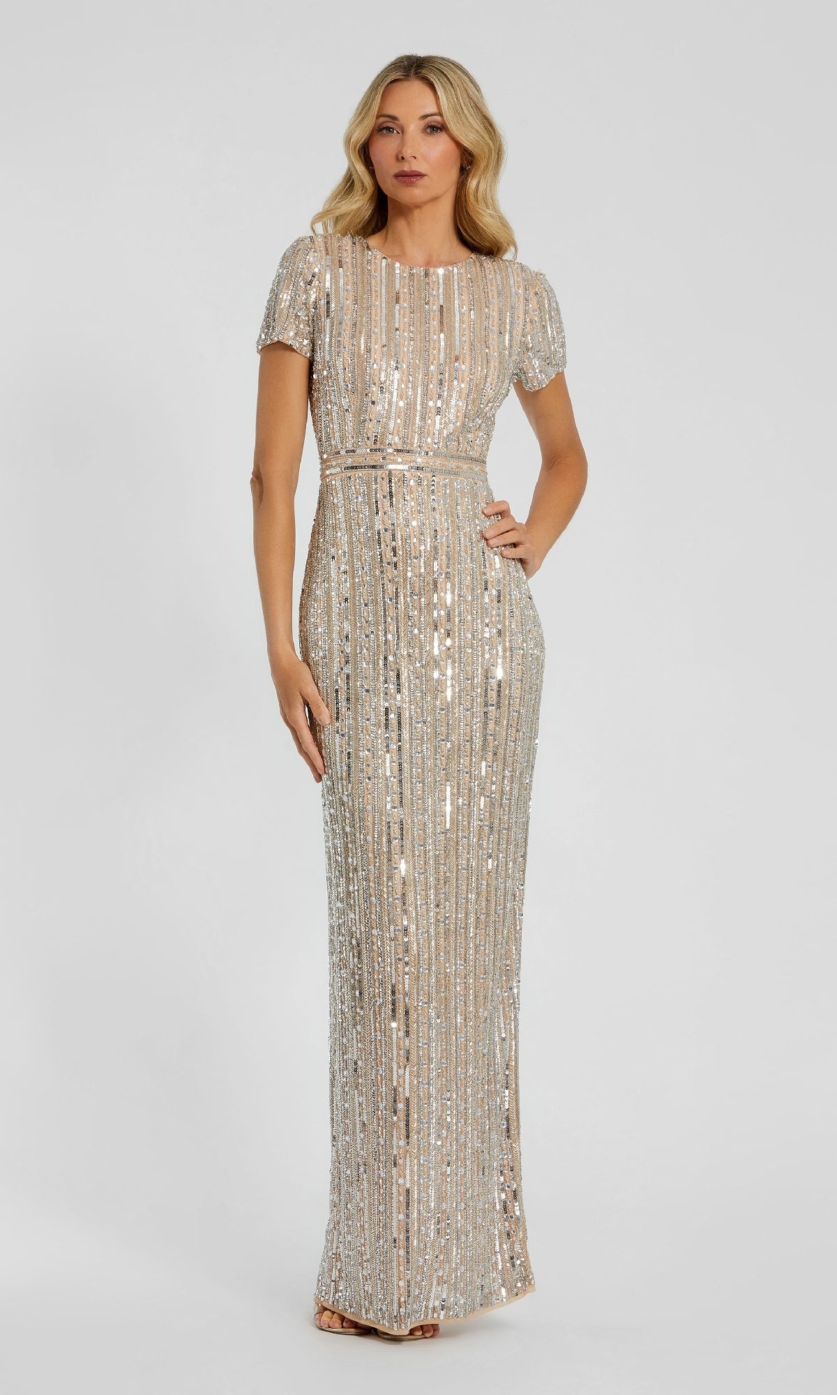 A woman stands against a plain light background, hands at her sides, wearing the Mac Duggal 93829 long formal dress with short sleeves, floor-length design, and vertical linear sequins.